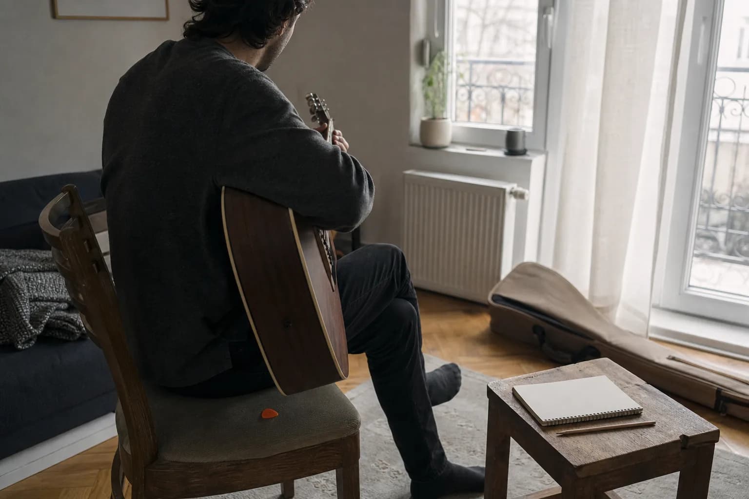 Un adult exersează la chitară acustică într-un colț liniștit de apartament